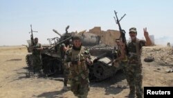 FILE - Iraqi Shiite militia fighters celebrate, near the wreckage of a tank belonging to Islamic State militants, after breaking a long siege of Amerli by Islamic State militants, September 2, 2014.