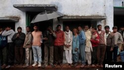 FILE - Voters take shelter from rain as they stand in a queue to cast their ballot at a polling station in Ayodhya during the state assembly election in the northern Indian state of Uttar Pradesh.