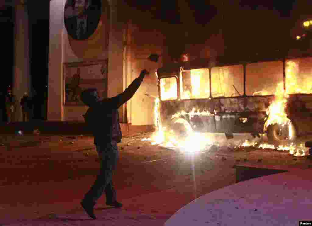 A pro-European integration protester throws a projectile past a burning police van during a rally near government administration buildings, Kyiv, Ukraine, Jan. 19, 2014.