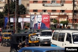 FILE - People and vehicles are seen near a poster of Egypt's President Abdel-Fattah al-Sisi for the upcoming presidential election, which reads "Yes, All of us with you for Egypt," in Cairo, Feb. 28, 2018.