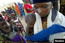 FILE - A woman holds her son, who is wearing a red bracelet indicating that he is severely malnourished, at the village of Darbani in northwestern Niger.