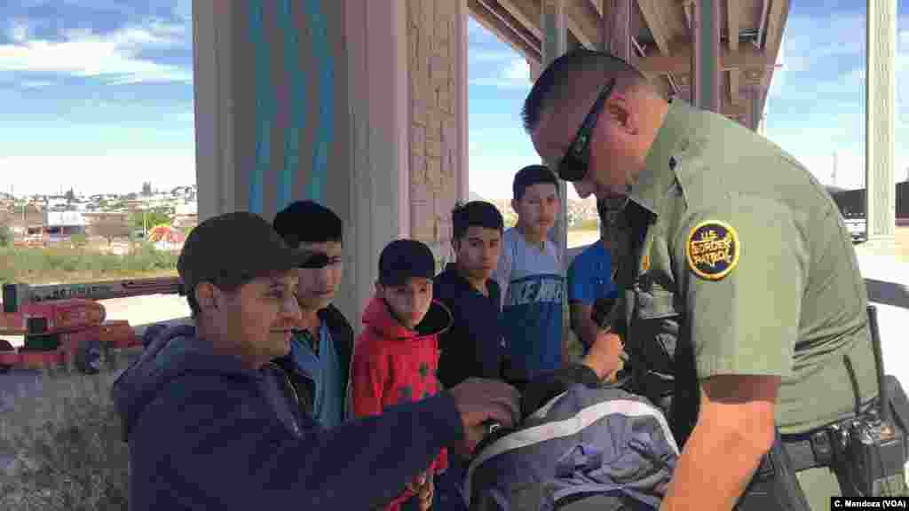 U.S. Customs and Border Patrol agents check migrants&#39; belongings. This group of Guatemalan migrants, which includes a child, wait to be processed by an agent, April 9, 2019. C. Mendoza/VOA News