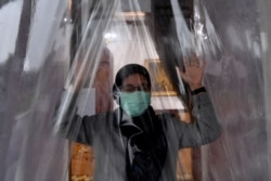 Seorang perempuan mengenakan masker masuk ke dalam ruang disinfektan untuk mencegah penyebaran virus corona COVID-19 di Surabaya, Jawa Timur, Senin, 23 Maret 2020. (Foto: Antara via Reuters)