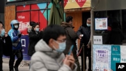 People wearing face masks to help curb the spread of the coronavirus use smartphones to scan their health code and get temperature check before entering a shopping mall in Beijing, Jan. 14, 2021.