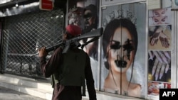 FILE - A Taliban fighter walks past a beauty salon with images of women defaced using spray paint in Shar-e-Naw in Kabul. 