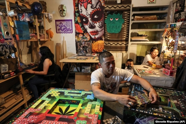 Diego Gonzalez, center, holds a pack of game pieces for poleana alongside designer Carolina Duran, left, and Dana Lopez, his partner, with their son Kevin in the State of Mexico, Mexico, Friday, Oct. 25, 2024. (AP Photo/Ginnette Riquelme)