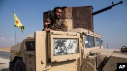 Seorang Kurdi anggota Pasukan Demokrat Suriah (SDF) siaga dengan senjata di atas sebuah kendaraan militer di Suriah. 
