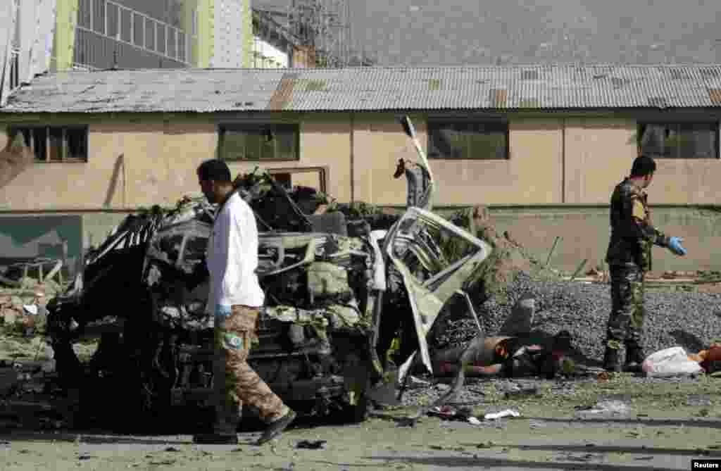 Afghan security personnel stand near a mangled vehicle as they investigate a suicide bomb attack, Kabul, Afghanistan, September 18, 2012. 