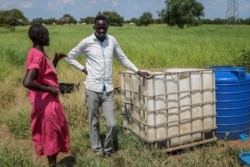 Residents stand next to a white container previously used for hazardous chemicals that was then used for several years to hold drinking water before the oil company put a stop to the practice, near Paloch, South Sudan, Oct. 1, 2018.