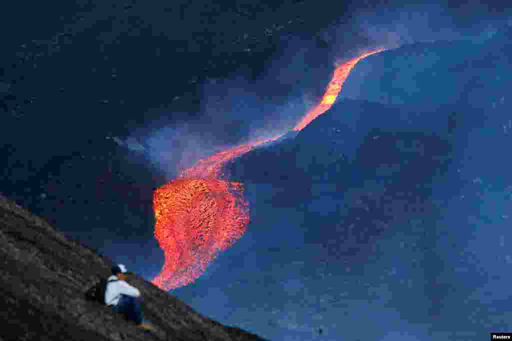 A man sits as red hot lava flows during an eruption of the Pacaya volcano at San Vicente de Sales municipality in the Escuintla region, Guatemala.