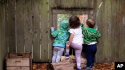 FILE - Children peer out a screened window in the fence at a child care center in Seattle, Aug. 27, 2018. Child care remains a obstacle for many women running for political office.