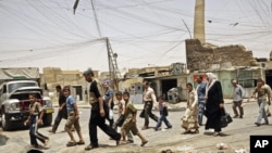 FILE - residents walk past the tilted minaret of al-Nuri mosque — also known as the Great Mosque — in Mosul, Iraq.