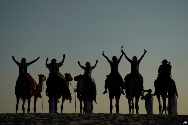 People pose for a photo atop camels in Mesaieed, Qatar, Nov. 26, 2022. Throngs of World Cup fans in Qatar looking for something to do between games are leaving Doha for a classic Gulf tourist experience: riding a camel in the desert. But the sudden rise in tourists is putting pressure on the animals, who have almost no time to rest between each ride. (AP Photo/Ashley Landis)