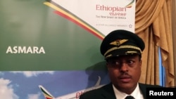 Kapteni wa shirika la ndege la Ethiopia Yoseph Hailu akiwa karibu na tangazo la safari za Asmara wakati wa kuadhimisha sherehe za kuanzisha safari hizo Uwanja wa ndege wa Ababa, Addis Ababa, Ethiopia Julai 18, 2018. 