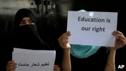 FILE - Afghan girls hold illegal protest signs to demand the right to education, in a private home in Kabul, Afghanistan, on Aug. 2, 2022.