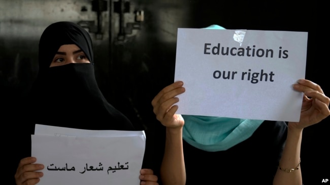 FILE - Afghan girls hold illegal protest signs to demand the right to education, in a private home in Kabul, Afghanistan, on Aug. 2, 2022.