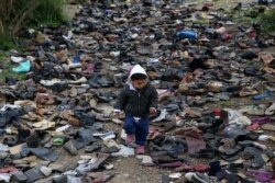 FILE - A boy walks among pairs of shoes at the premises of an NGO next to the Moria camp for refugees and migrants, on the island of Lesbos, Greece, March 9, 2020.