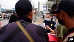 FILE - A U.S. Customs and Border Protection officer examines paperwork of migrants waiting to cross into the United States to request asylum, in Tijuana, Mexico, July 5, 2021.