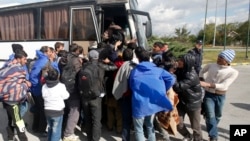 Migrants board a bus at a local gas station near the town of Indjija, about 40 kilometers (24 miles) north of the Belgrade, Oct. 5, 2016.