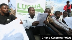 Les jeunes du mouvement citoyen Lutte pour le changement (LUCHA) assis par terre devant le quartier général de la Monusco lisent un mémo, à Goma, Nord-Kivu, RDC, 26 octobre 2017. (VOA/Charly Kasereka)