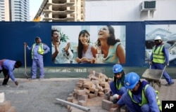 Laborers install paving stones in front of an advertisement for luxury real estate, in the Marina district of Dubai, United Arab Emirates, March 26, 2015.