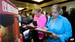 FILE - Job seekers fill out employment applications at a job fair in Miami Lakes, Florida.
