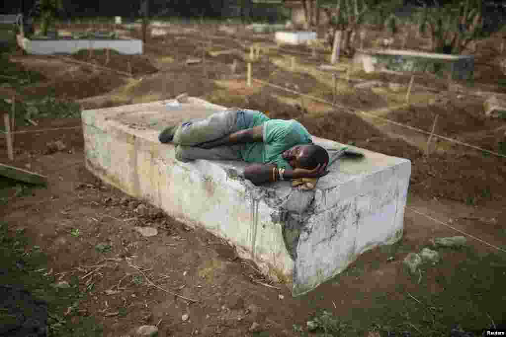Un fossoyeur s&rsquo;en dort sur une tombe près de l&rsquo;endroit où des victimes d&#39;Ebola sont enterrées dans un cimetière de Freetown, 17 décembre 2014. REUTERS / Baz Ratner