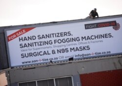 A worker attaches a billboard, advertising sales of hand sanitizer and masks, to a building ahead of a 21 day lockdown aimed at limiting the spread of coronavirus disease (COVID-19), in Cape Town, South Africa, March 25, 2020.