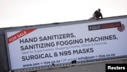 FILE - A worker attaches a billboard, advertising sales of hand sanitizer and masks, to a building ahead of a 21 day lockdown aimed at limiting the spread of coronavirus disease (COVID-19), in Cape Town, South Africa, March 25, 2020. 