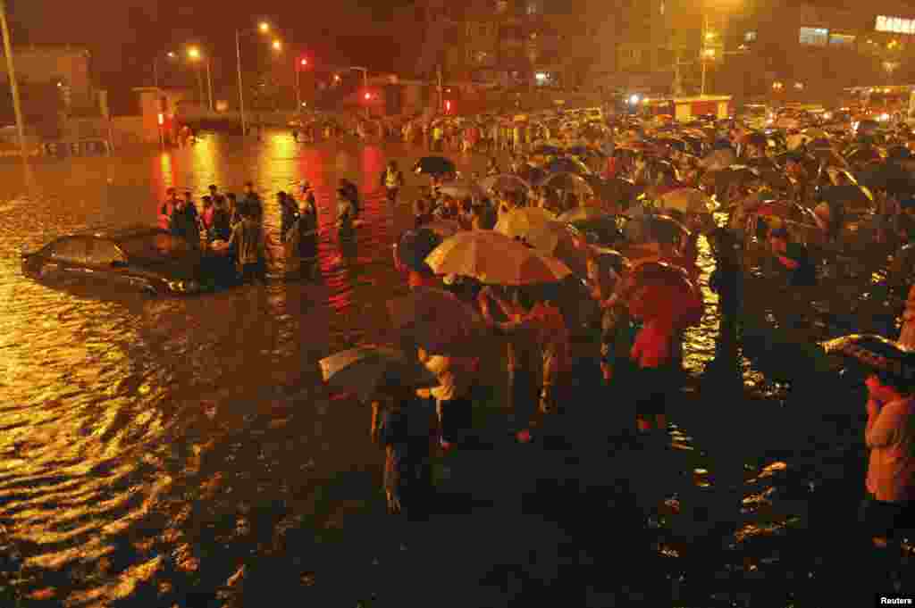 在北京广渠门立交桥附近，救援人员和居民站在一旁观望一辆从街道积水中被拖出的小汽车(7月21日)。