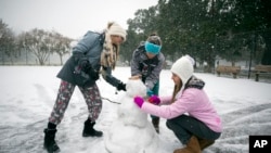 Children from the Hoffman and Lynns families build a snowman on the public basketball courts in Forsyth Park, Jan. 3, 2018, in Savannah, Georgia.