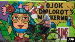 Seorang pengendara sepeda melewati mural yang memperingatkan warga tentang pandemi Covid-19 di sepanjang jalan di Surabaya, 30 November 2020. (Foto: Juni Kriswanto / AFP)