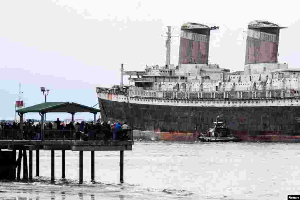 Onlookers watch as SS United States, a retired American ocean liner, is towed out to sea on the Delaware River, on her way to Alabama where she is intended to be sunk to create an artificial reef, in Philadelphia, Pennsylvania, Feb. 19, 2025. The ocean liner was built during 1950 and 1951 for United States Lines.