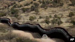 FILE - A Customs and Border Control agent patrols on the U.S. side of a razor-wire-covered border wall along the U.S.-Mexico border, east of Nogales, Arizona, March 2, 2019.