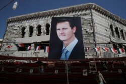 FILE - A man walks past a banner depicting Syrian President Bashar al-Assad, in Douma, outside Damascus, Syria, Sept. 17, 2018.