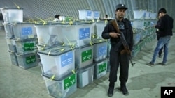 An Afghan police officer stands guard as election workers (R) note serial numbers of ballot boxes at a warehouse of the Independent Elections Commission warehouse in Kabul, April 6, 2014.