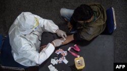 Seorang petugas kesehatan (kiri) mengambil sampel darah dari seorang pengendara motor yang melanggar Pembatasan Sosial Berskala Besar (PSBB) di sebuah kantor polisi di Surabaya, 3 Mei 2020. (Foto: AFP)