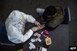 Seorang petugas kesehatan (kiri) mengambil sampel darah dari seorang pengendara motor yang melanggar Pembatasan Sosial Berskala Besar (PSBB) di sebuah kantor polisi di Surabaya, 3 Mei 2020. (Foto: AFP)