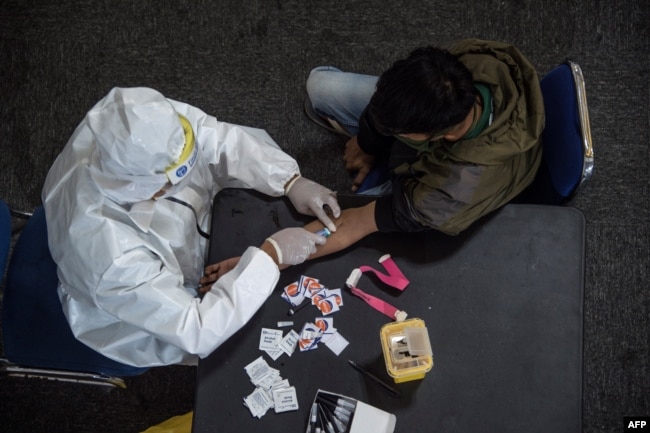 Seorang petugas kesehatan (kiri) mengambil sampel darah dari seorang pengendara motor yang melanggar Pembatasan Sosial Berskala Besar (PSBB) di sebuah kantor polisi di Surabaya, 3 Mei 2020. (Foto: AFP)