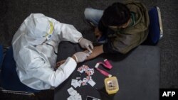 Seorang petugas kesehatan (kiri) mengambil sampel darah dari seorang pengendara motor yang melanggar Pembatasan Sosial Berskala Besar (PSBB) di sebuah kantor polisi di Surabaya, 3 Mei 2020. (Foto: AFP)