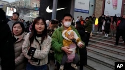 FILE - A man carries a child at a shopping mall in Beijing, Dec. 30, 2023. China’s population dropped by 2 million people in 2023 in the second straight annual drop as births fell and deaths jumped. (AP Photo/Ng Han Guan)