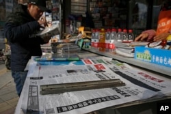 FILE - A man arranges magazines near newspapers with the headlines of China outcry against U.S. on the detention of Huawei's chief financial officer, Meng Wanzhou, at a news stand in Beijing.