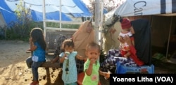 Suhu yang panas di dalam tenda membuat dua orang ibu dan anak-anak mereka beraktifitas di luar tenda pada siang hari, 18 Juni 2019.(Foto: Yoanes Litha/VOA)