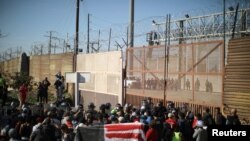 Les migrants, qui font partie d'une caravane de milliers de personnes en provenance d'Amérique centrale et se dirigeant vers les États-Unis, observent des patrouilleurs de frontière américains à travers le mur frontière entre les États-Unis et le Mexique, le 25 novembre 2018.
