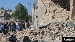 FILE - Residents look at the damage by what activists said was a barrel bomb dropped by forces of Syria's President Bashar al-Assad, in the old city of Aleppo, May 31, 2015.