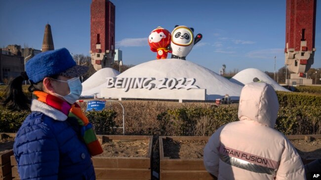People wearing face masks to protect against coronavirus look at a display of the Winter Paralympic mascot Shuey Rhon Rhon, left, and Winter Olympic mascot Bing Dwen Dwen near the Olympic Green in Beijing, Jan. 12, 2022.