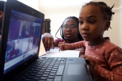 Lear Preston, 4, who attends Scott Joplin Elementary School, participates in her virtual classes as her mother, Brittany Preston, background, assists at their residence in Chicago's South Side, Wednesday, Feb. 10, 2021. (AP Photo/Shafkat Anowar)