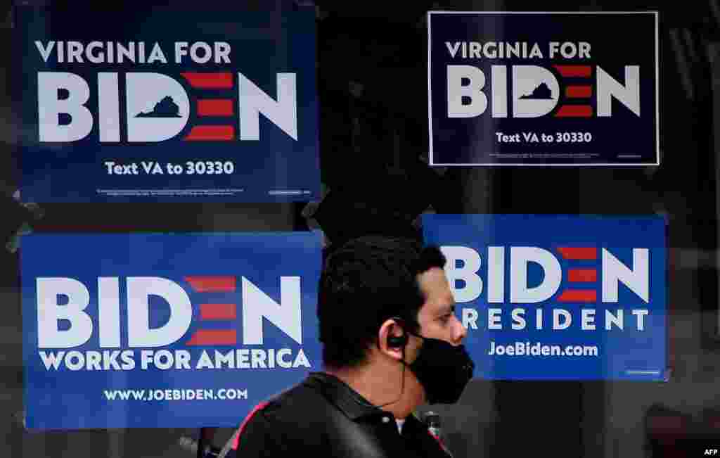 Човек со маска минува крај постери со поддршка за Џо Бајден во Александрија, Вирџинија. (Olivier DOULIERY / AFP)