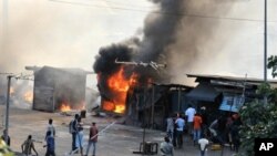 People stand next to stores set on fire during clashes between supporters of Alassane Dramane Ouattara and soldiers of the FDS, loyal to outgoing president Laurent Gbagbo, in the Attecoube neighborhood, in Abidjan, February 24, 2011.