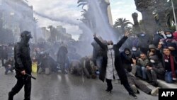 Demonstran mengacungkan tanda "V" (kemenangan) setelah polisi menembakkan meriam air dalam aksi protes di Tunis, Jumat (14/1).